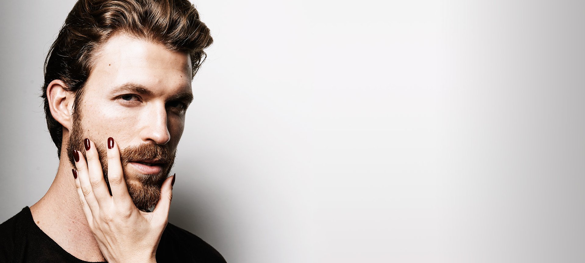 Attraktiver Mann mit Frauenhand am Bart